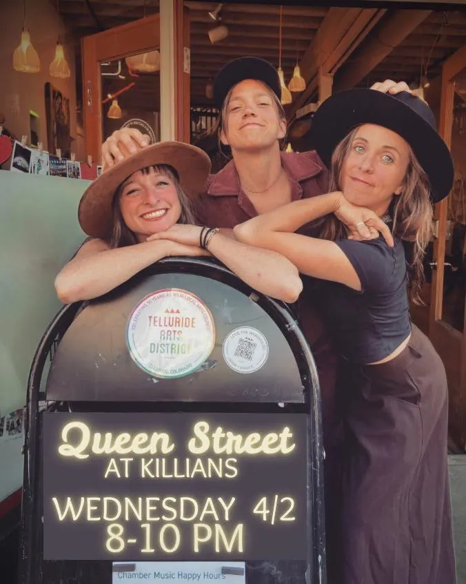 Three smiling guests posing behind the Queen Street at Killians event sign in Spearfish, SD